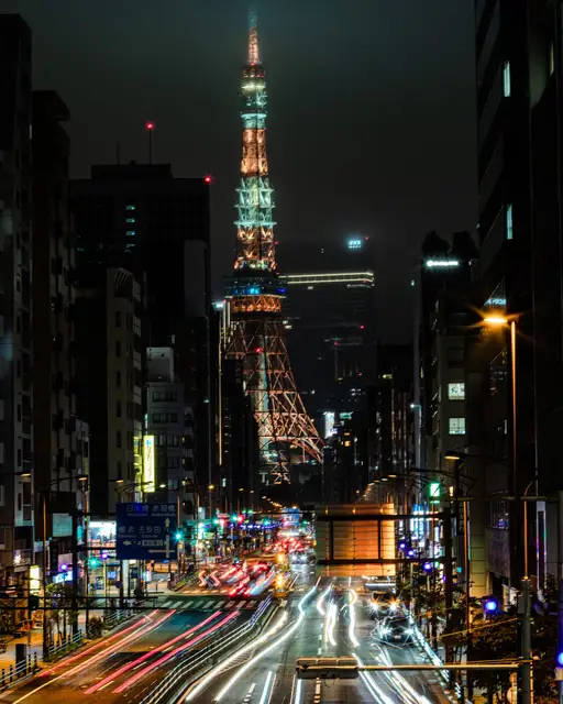 ビル街の大通りの正面にそびえる、ライトアップされた東京タワーと車の光跡